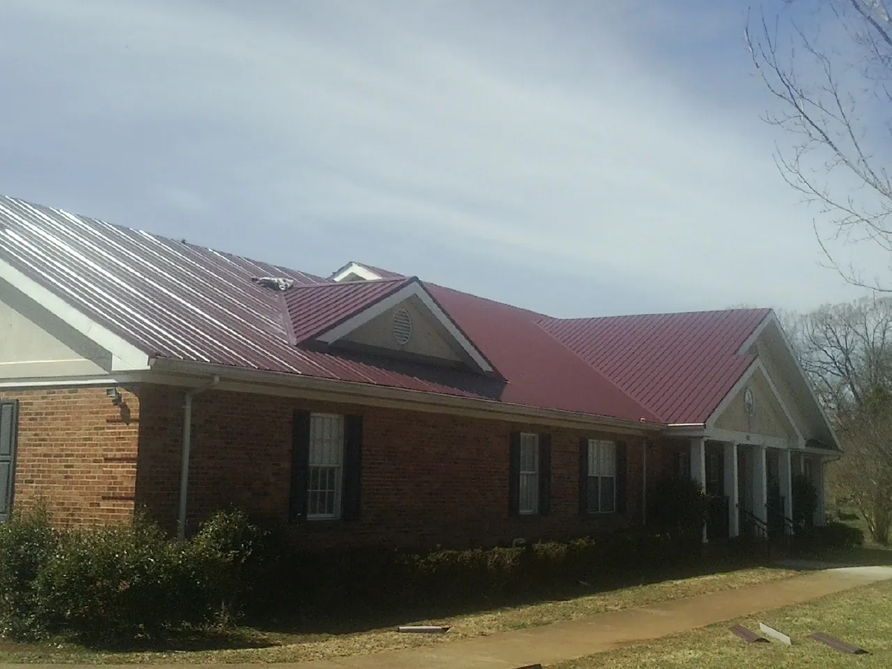 Red metal roof with gabled entries on a long brick building, from a Hail Damage Roof Repair job in Rittman