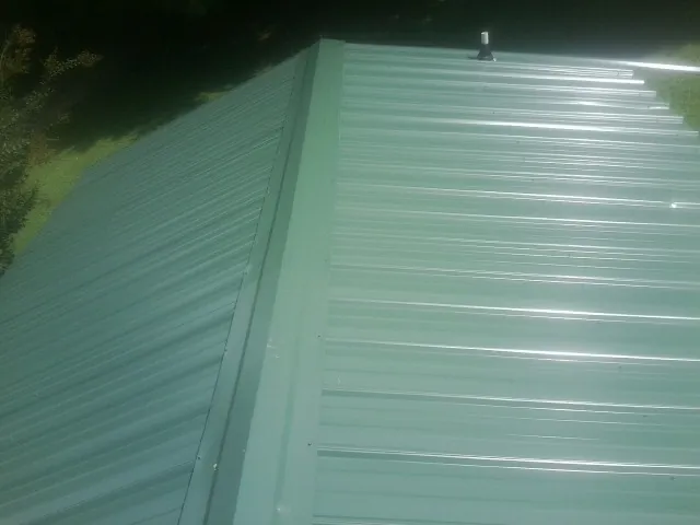 New green metal panels meeting at the ridge of a roof — Flat Roof Repair work by our crew in Rittman