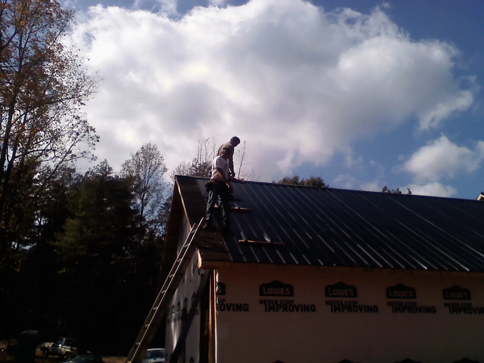 Roofer fastening dark metal panels high against a cloudy sky, from a Roof Inspection job in Rittman