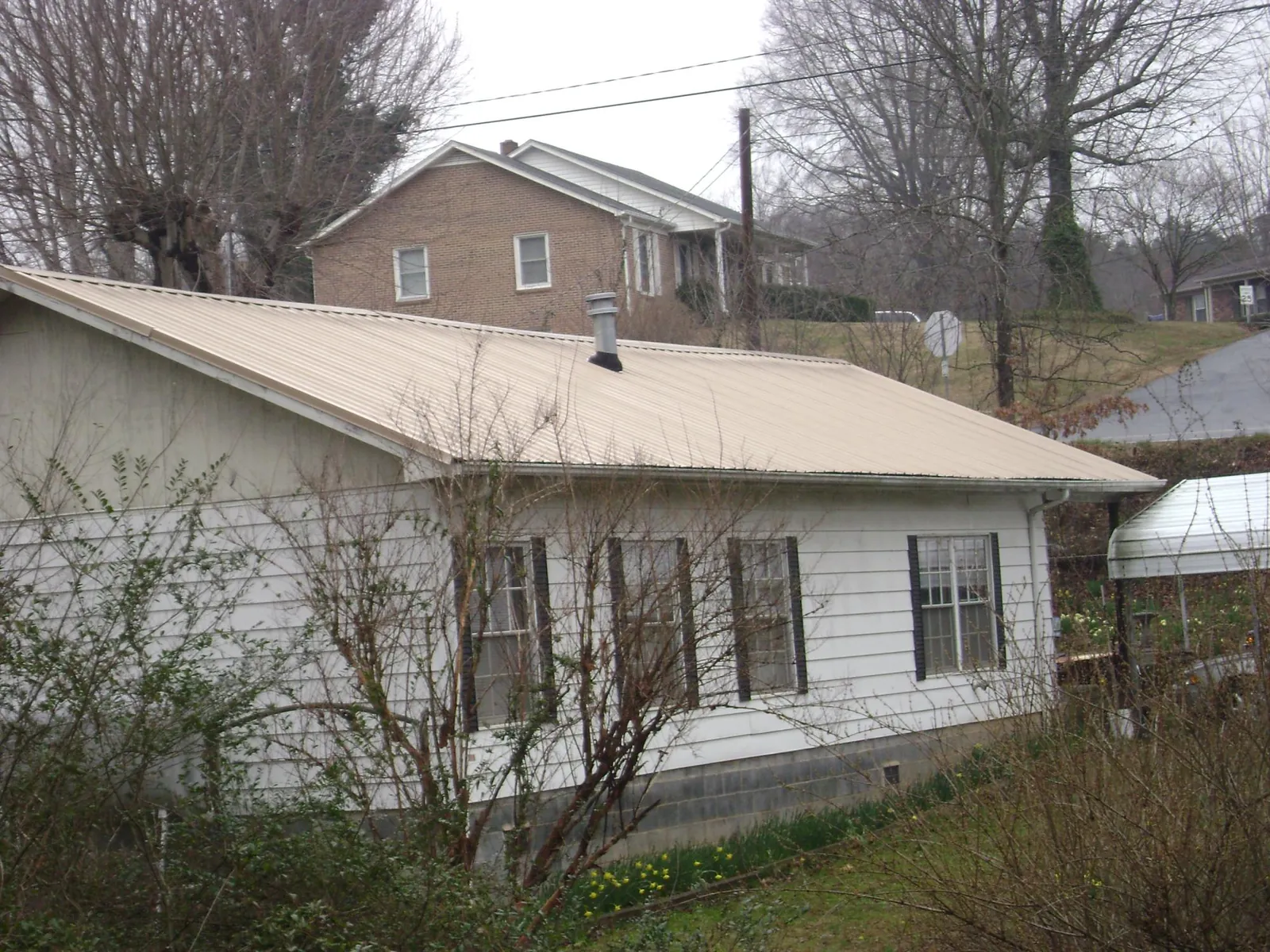 Tan metal roof on a white sided house set into a hillside — Commercial Roofing by Roofing Brothers in Rittman